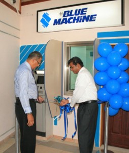 CEO of the CJIA, Ramesh Ghir (right) is assisted by Managing Director of Republic Bank, Edwin H. Gooding, as he cuts the ribbon that marks the ATM open. 