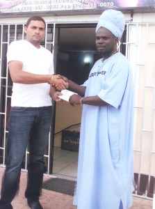 I Salam (right) collects the cash donation  form the proprietor of Pure Diamond  last week at their Bartica location.