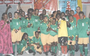 The victorious Uprising U-15 players pose with the Coca-Cola trophy and beverages along with Banks DIH officials Jennifer Khan (partly hidden centre) and Carlton Joao (right back row).