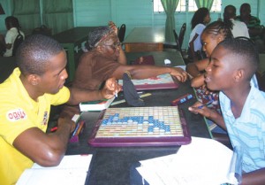 Leon Belony (left), one of the top rated scrabble players, explains to one of  the students, Omari Dunn, his reason for making a particular move.  Yvonne Murray, (left of Belony) also assists Shanice Bourne,  another novice, in the acquisition of valuable tips.