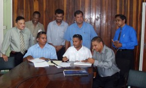 Priudanmanlall Ramlall (sitting right) signs the contract, while Bridgepaul Shivnath (sitting right) and GCB executives witness the signing.