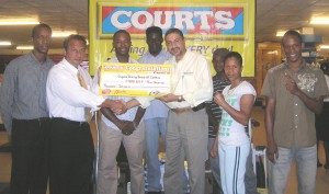 GBBC President, Peter Abdool (left) accepts the sponsorship check from Mr. DeHaas in the presence of Holland (2nd L), Pernell Cummings (extreme left), Rogers (3rd L), Leon Moore (extreme right), Shondell Alfred (2nd R) and Paul Lewis Jnr, (partially hidden). 