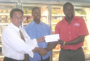 Christopher Franklyn (right) hands over the check to Mr. Abdool in the presence of Carwyn Holland. 