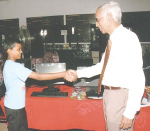Executive Director of Laparkan, Vibert Parvatan, congratulates first prize winner, Ricardo Subramani, of Helena Primary School, who received a complete computer system.