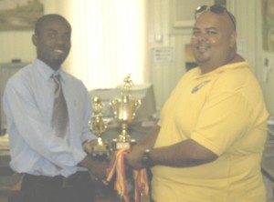 Insurance Brokers Guy Ltd staffer Lomell Johnson presents the trophies to Yamaha Caribs Treasurer Troy Yhip (right) at the Company’s location recently.