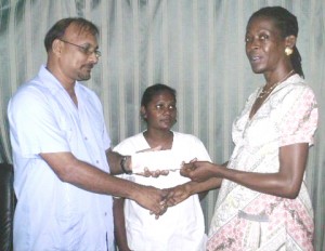 Dr. Ramesh Sugrim presenting the cheque to Maxine Williams in the presence of another member of the group.