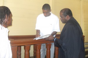 Former Army Lieutenant Diallo George signs the recognizance for his release in the presence of his attorney Nigel Hughes and his father Patrick George. 