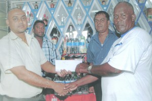 Sales Manager of Banks DIH, Joshua Torrezao (left), hands over the sponsorship cheque to Berbice coach, Randolph Roberts, while Supervisors Joseph Taylor and Nandram Basdeo look on.