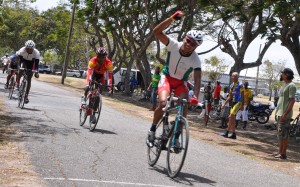 Alonzo Greaves punches the air in triumph as he approaches the finish line ahead of Robin Persaud, Marlon Williams and Enzo Matthews in yesterday’s feature at the National Park. (Franklin Wilson photo)  