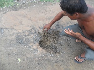 A resident pointing to a hole formed by the  leakage in the pipeline within the road.