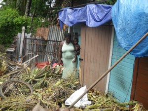 Joan Junior holds her two-year-old son, while the fallen tree remains in the yard and tarpaulin covers the roof of the house.  