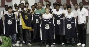 Banks DIH Executive, Carlton Joao (centre) and Marian Academy’s basketball team hold up some of the apparel that were handed over to them from the company yesterday as Coach, Chris Bowman (right) joins his team.