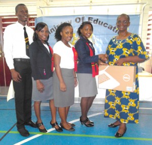 Senior Lecturer (Student Development), Ms Esther Utoh (at extreme right) hands over a laptop to a trainee teacher in the company of three others.
