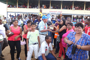 KMTC president Justice Cecil Kennard (left) presents the $1M and trophy to Mrs Dennis DeRoop of the simple Royal Stable for Score’s Even victory.