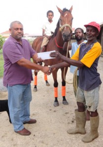 Businessman Fazal Habibulla (left) presents his sponsorship package at a simple ceremony at the Shariff Cattle ranch to one of the organizing assistants William Fraser. In the back ground is top horse Swing Easy with apprentice jockey Andy ‘Jugu’ Jameson.