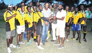 Golden Brook’s Dustani Barrow (right) hands over the winning trophy to Yamaha Caribs Captain Akeem Fraser in the presence of teammates and other sponsors representatives on Saturday. 