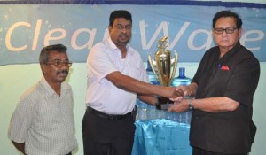 IPA CEO Lloyd Singh (left) presents the trophy to KMTC head Cecil Kennard in the presence of manager Bowhan Balkaran. 