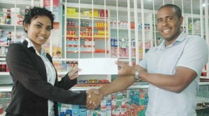 Accountant at The Medicine Chest Pharmacy on Middle Street, Arron Fraser, hands over their contribution to Director at Respect the Game Inc., Surika Danraj yesterday ahead of the Dec. 13 Charity Basketball Event at the Cliff Anderson Sports Hall. 