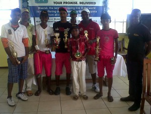  Outstanding Macorp players from left to right, Robin  Tiwari, Roy Cummings, Ivor Laudin, Kevin Dinanauth,  Vicky Baldeo (junior in red jersey) then Harrycharan  Danai, Jamal Mohamed and Macorp’s representative. 