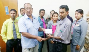 Bryan Baker of NBS New Amsterdam hands over sponsorship cheque to Hubern Evans in the presence of other staff members.