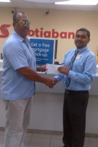 Scotiabank Business Banking Manager, Mohamed Azim, hands over sponsorship cheque to Hubern Evans (left), Head Coach of YWCC.