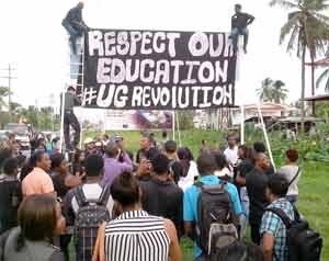Students drape the University of Guyana sign at the Railway Embankment as others look on