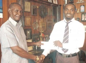 Supervisor at IBGL, Lomell Johnson (right) hands over the company’s sponsorship cheque to Sports Management’ Claude Bennett.