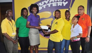 A representative of the Guyana Lottery Company hands over the sponsorship cheque to national rugger Andrea Lashely in the presence of GRFU officials yesterday.