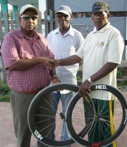 Minister Singh (left) and Aaron Abrams present the wheels to coach Randolph Roberts. 