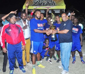 Guyana Beverages Inc General manager Robert Selman (right) hands over the winning trophy to Sparta Boss Captain in the presence of teammates and Petra Organisation Co-Director Troy Mendonca Tuesday night at the GFC ground.