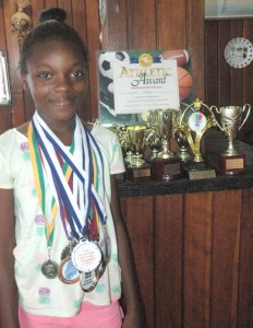 Abosaide Cadogan poses with some of her trophies and medals at home.