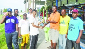 Captain of Floodlights XI Dharam Persaud (left) accepts the trophy from Coach Lyndon Wilson in the presence of team mates and organizer Trevor Wharton (second from right).