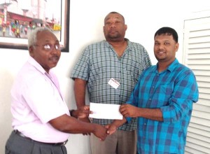 Human Resources Manager of Sentinel Bromwell Gordon (Left) hands over the cheque to RHTY&SC member Mark Papannah in the presence of Hilbert Foster. 