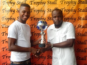 Esan Pyle of the Organising Committee (right) collects one of the trophies on offer from a Representative of the Trophy Stall. 