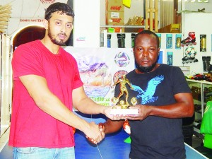 Esan Pyle of the Organising Committee (right) collects one of the trophies on offer from a Representative of West Indian Sports Complex yesterday. 