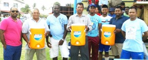 Representatives pose with their coolers in the presence of West Indies Under-19 captain Shimron Hetmyer and other cricketers.