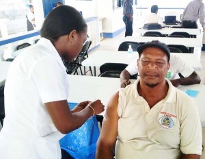 A GWI employee receives a vaccine from a Public Health Ministry representative.