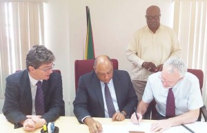 John McKenna of Tullow Oil signs the agreement as Minister of Natural Resources, Raphael Trotman (centre), British High Commissioner to Guyana, Greg Quinn (left) and Newell Dennison, acting Commissioner, GGMC (standing) look on. 