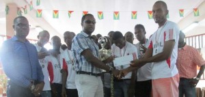 Banks GT Beer Brand Manager Mr. Geoffrey Clement (left) hands over the winners’ $800,000 first prize to Marlon Maxius, captain of Federal Winners Connection FC, while his teammates and UDFA boss Sharma Solomon (left) look on.