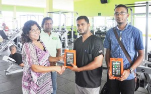 Fitness 53 Gym Manager Darlene Harris presents the Tablet to Ravi Persaud, while Neion Barry (right) and Gym attendant Toni share the moment.