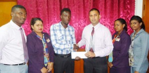 Former national youth player Linden Austin (left) collects sponsorship cheque from NBS Berbice Manager Rana Persaud in the presence of other staff members.