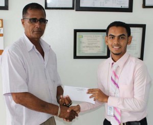 Mr. Deon Esau employee of Republic Bank Corriverton Branch hands over the donation cheque to UCCA President Mr. Dennis De Andrade.