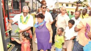 President David Granger assists little Ms. Fieona Mohamed, as she cuts the ribbon to commission the bus at Rose Hall, as Minister of Social Cohesion, Ms. Amna Ally  and Donor Nazrudeen Jumbo Jet Mohammed look on.