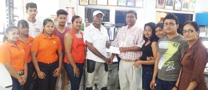 Managing Director of Nand Persaud and Company Limited Mohin Persaud (right) presents a cheque to Assistant organiser Compton Sancho at the Company’s No36 Village Corentyne location as staff members share the moment. 