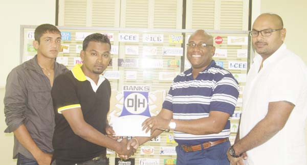 Beverages manager of Banks DIH Clive Pellew (right) hands over the cheque to Shabber Baksh in the presence of Branches Controller Gavin Jodha (far right) and BCC U19 captain Zameer Inshan.