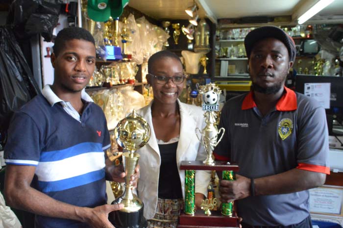 Ms. Marva Langevine (center) displays some of the trophies along with the Trophy Stall Rep. at left and Coach Wayne Dover.