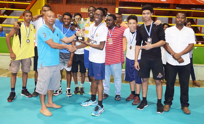 Queen’s Colege volleyball: Caption- GVF President John Flores (left) hands over the winning trophy to Queen’s College Captain Omari Joseph in the presence of DVA President Trevor Willams (right) and teammates yesterday. 