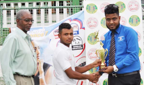 Man-of-the-match Ronaldo Renee collects his prize from Hand-in-Hand representative Mikhail Da Silva in the presence of match referee Grantley Culbard. 