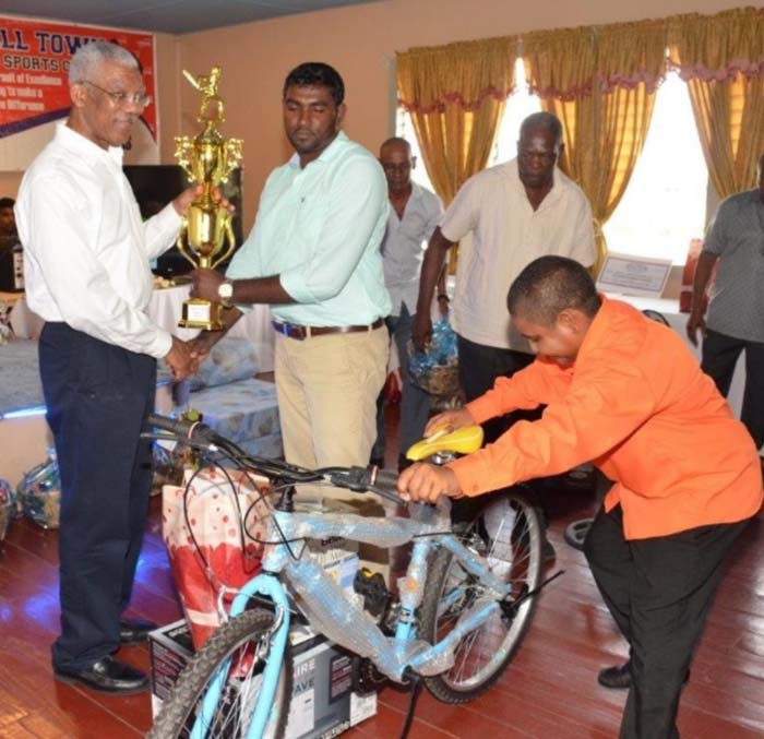 Cricketer of the year Khemraj Mahadeo Receives prizes from President Granger as Worker of the Year Simon Naidu sets up Mahadeo’s cycle, part of his collection of prizes.