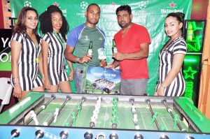 Danesh Persaud (second, right) collects a miniature Foosball table and tickets to the Finals Viewing Party from Heineken Brand Assistant, Keiron Brathwaite Friday night at Seepaul’s Bar, Kitty in the presence of Heineken models. 